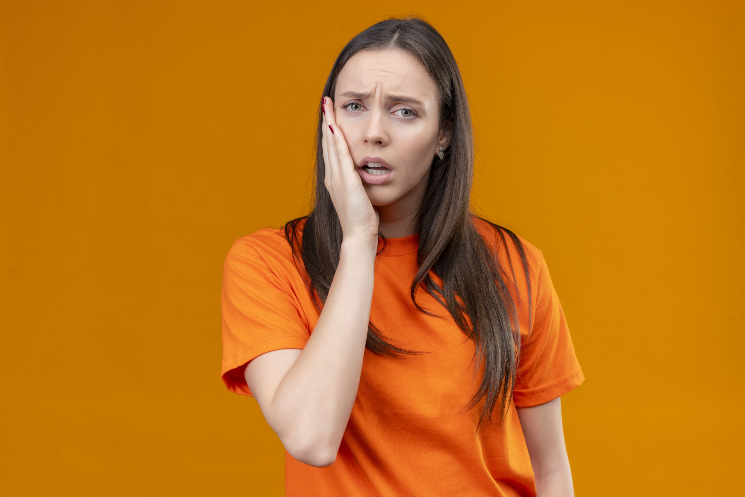 young beautiful girl wearing orange t-shirt looking unwell touching her cheek feeling toothache standing over isolated orange background